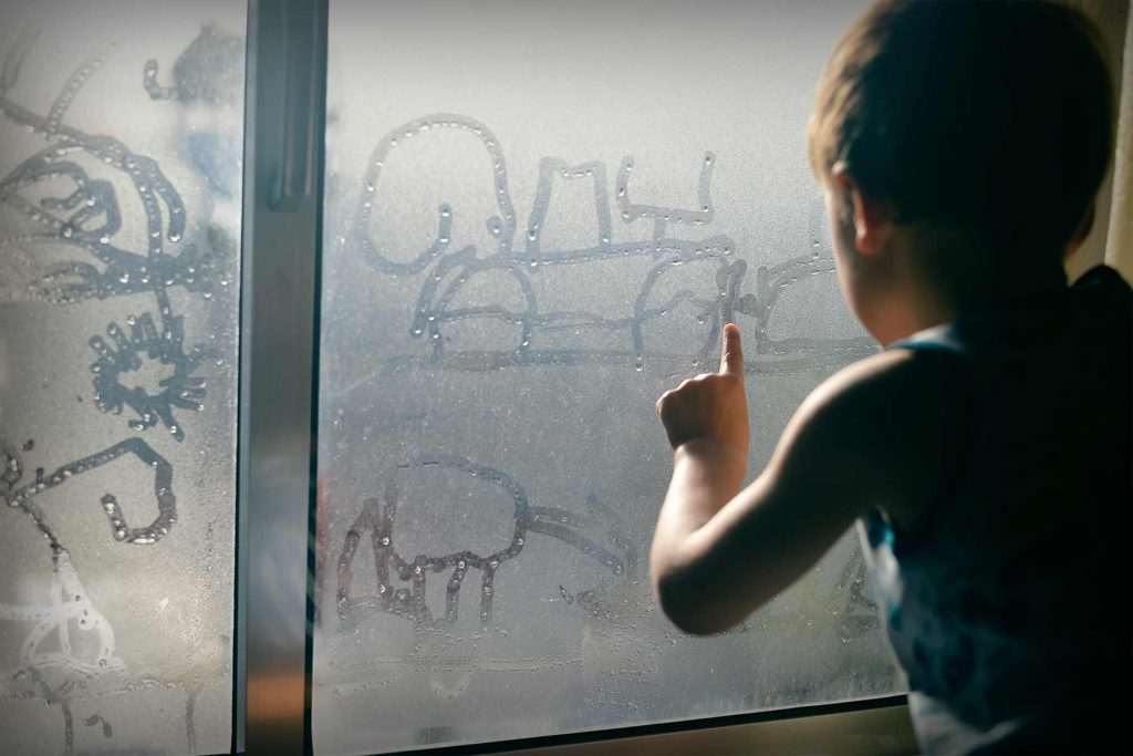 Child drawing with finger on a foggy window